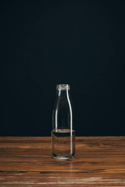 glass bottle with mineral water on brown table on black clipart