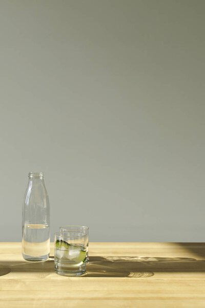 бутылка с минеральной водой и стекло с водой и огурцом на деревянном столе
