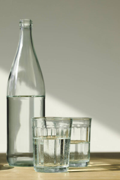 прозрачная бутылка и стаканы с минеральной водой на деревянном столе
