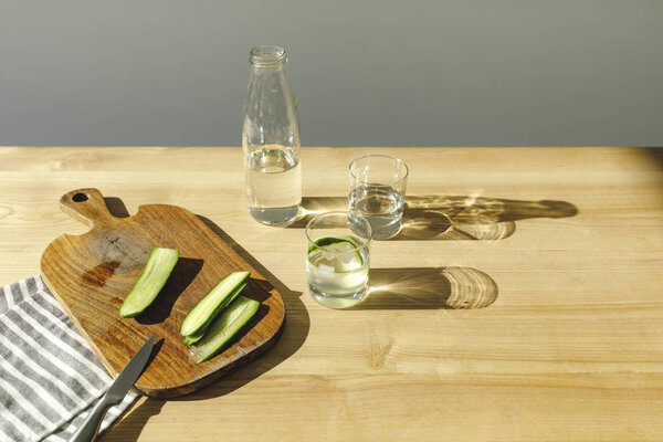 cut cucumbers on wooden board and mineral water on wooden tabletop 