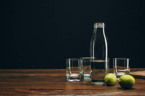 Bottle with water, glasses and limes on wooden tabletop