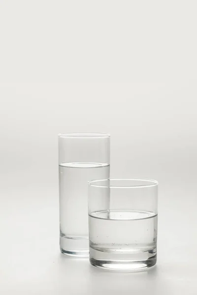 Dvě Různé Skleničky Klidnou Vodou Izolované Bílém — Stock fotografie