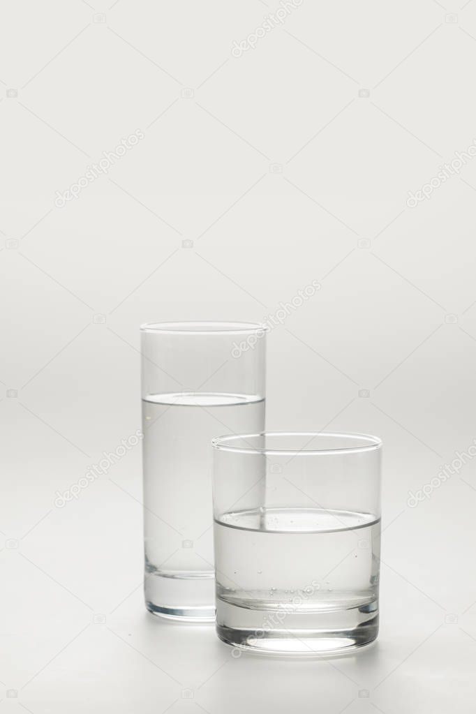 two different glasses with calm water isolated on white 