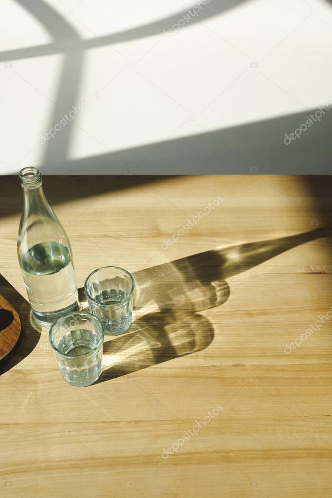 overhead view of transparent bottle and glasses with mineral water