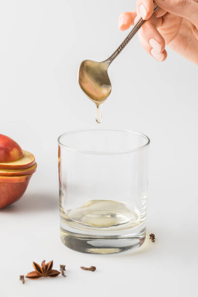 cropped shot of woman pouring honey in glass from spoon on white table