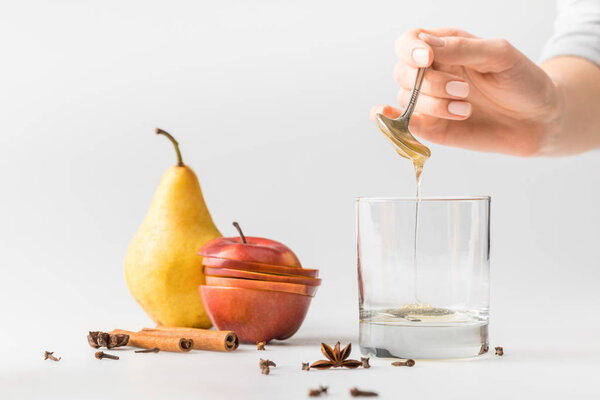 cropped shot of woman pouring honey in glass from spoon on white table