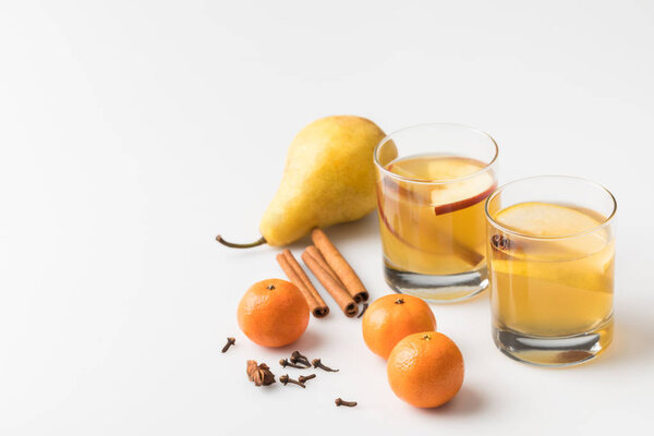 close-up shot of glasses of cider with pear and tangerines on white