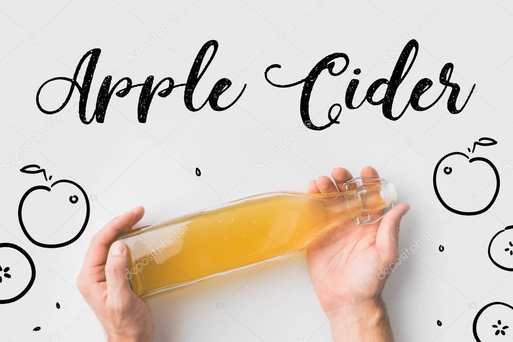 top view of person holding bottle of cider with hand drawn apples and lettering on white surface