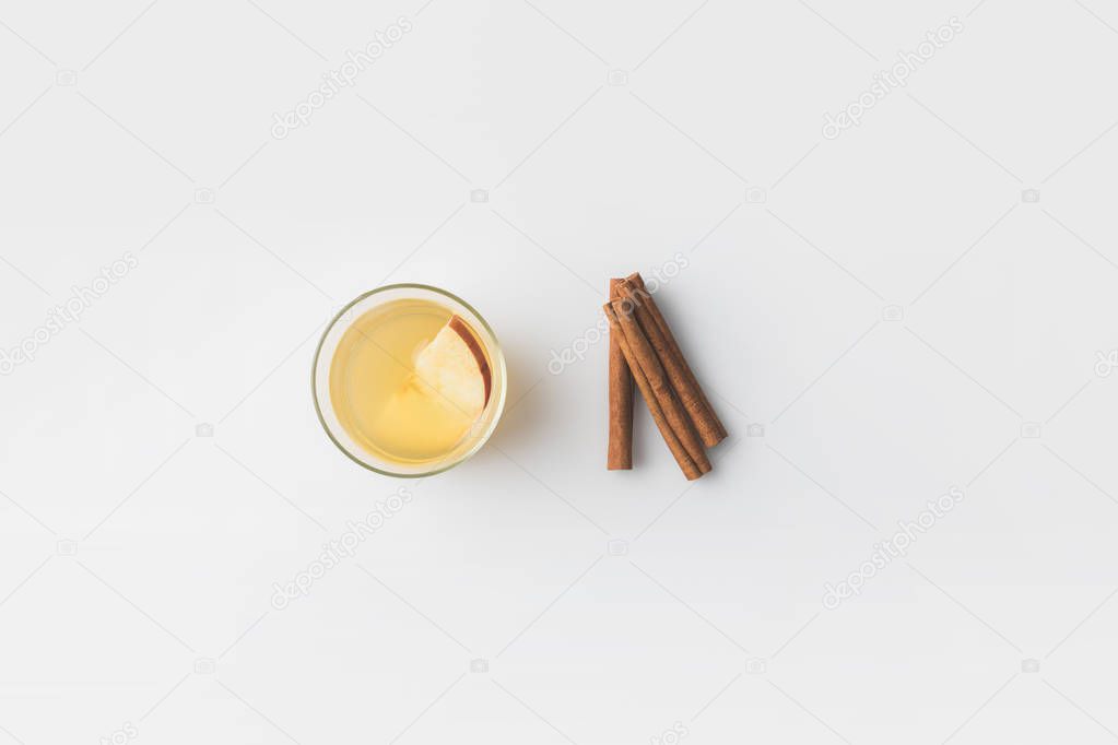 top view of glass of apple cider with cinnamon sticks on white surface