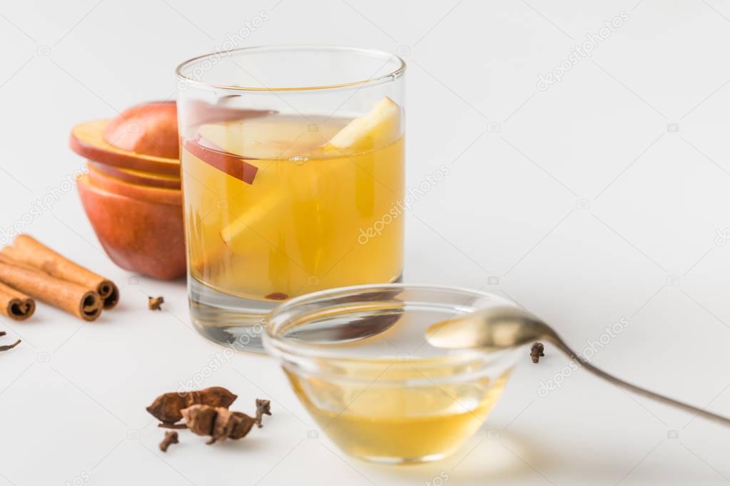 glass of apple cider and honey in bowl on white table