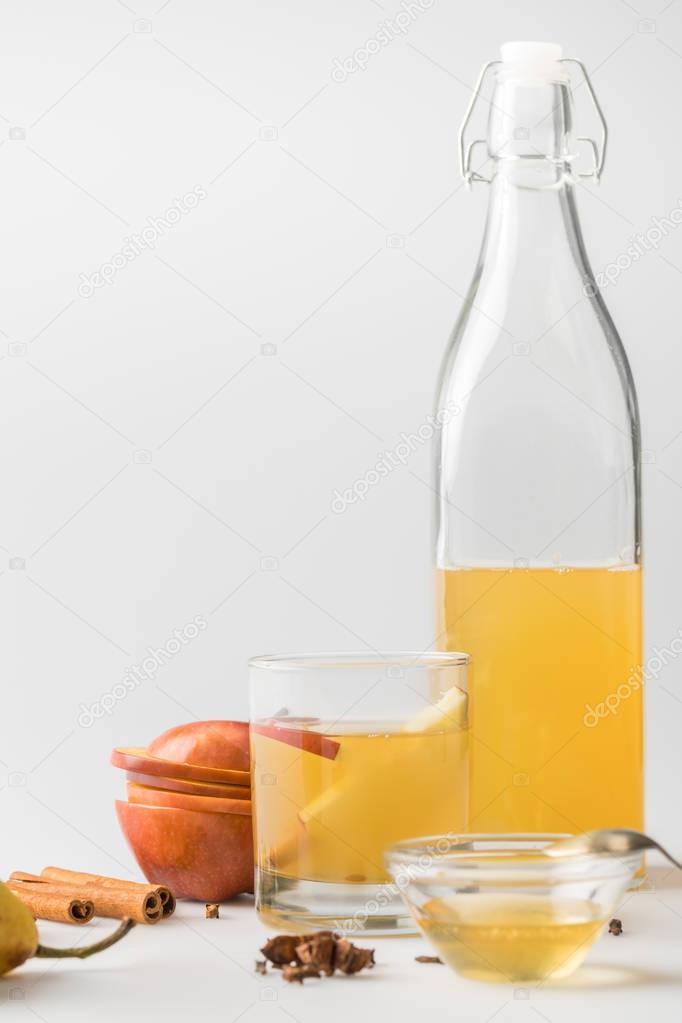 apple cider in bottle and glass with spices on white surface