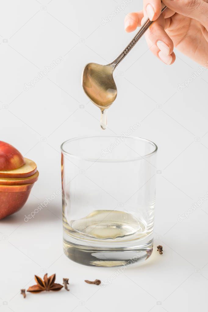 cropped shot of woman pouring honey in glass from spoon on white table