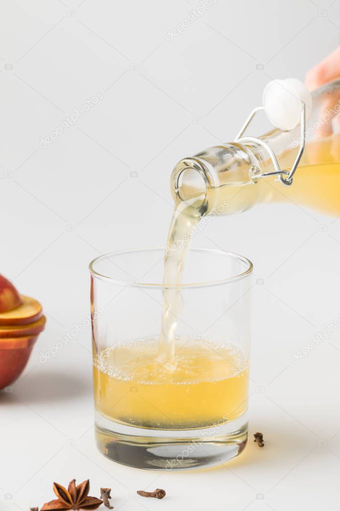 close-up shot of refreshing cider pouring in glass on white surface