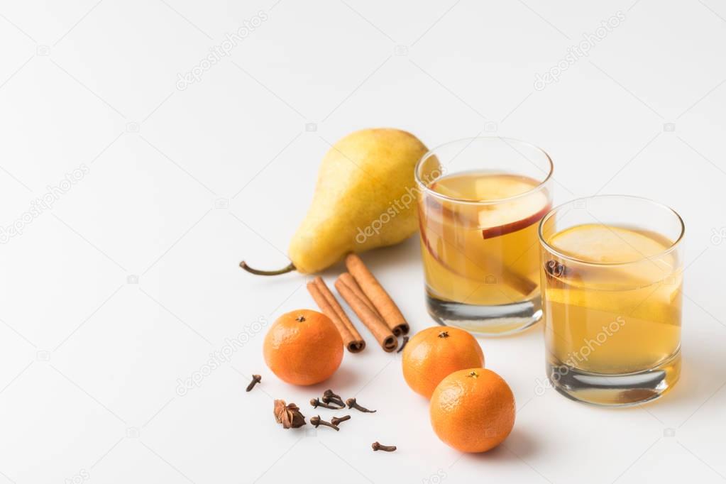 close-up shot of glasses of cider with pear and tangerines on white