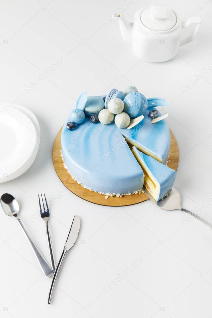 blue tasty cake on chopping board with teapot and plates isolated on white