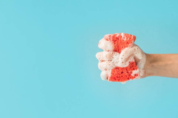 cropped view of hand holding washing sponge with foam, isolated on blue