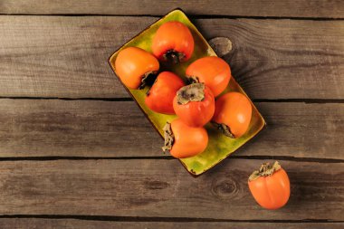 top view of persimmons on yellow bowl on striped wooden table clipart