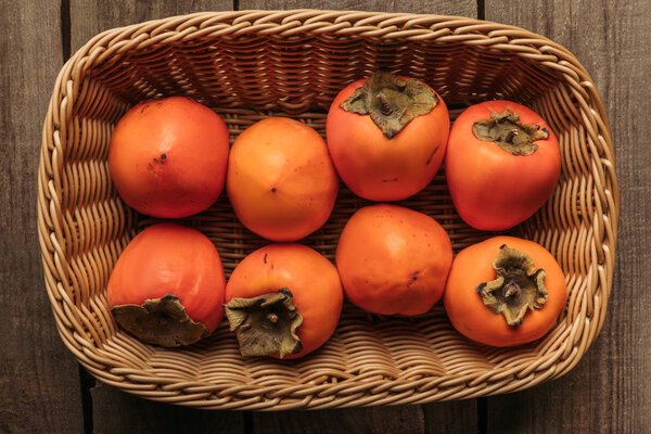top view of appetizing persimmons in straw basket on table