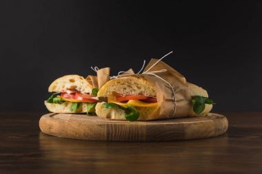 two cooked appetizing sandwiches with vegetables on wooden board clipart