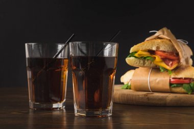 two glasses of cola on table and panini on wooden board clipart