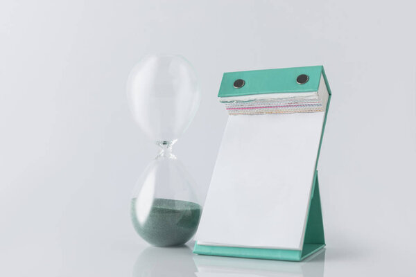 close up view of hourglass and empty calendar isolated on white
