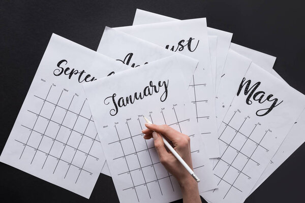 partial view of woman making notes in calendar isolated on black