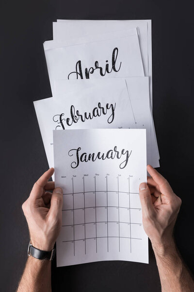 partial view of man holding calendar in hands isolated on black