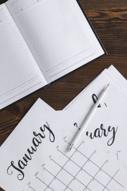 ahşap yüzey üzerinde boş not defteri, takvim ve kalem görünümü kadar kapatın