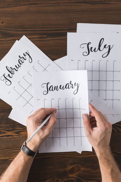 cropped shot of man making notes in calendar on wooden tabletop