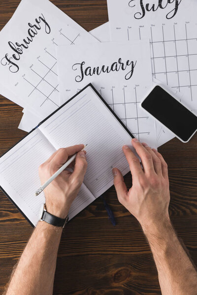 partial view of businessman making notes in notebook at table with calendar