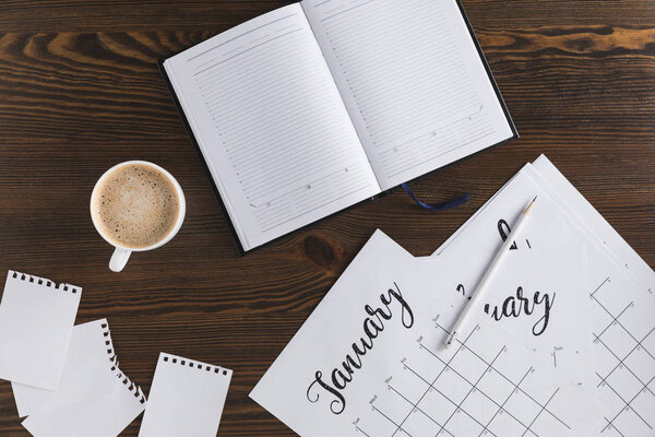 flat lay with empty notebook, calendar and cup of coffee on wooden surface