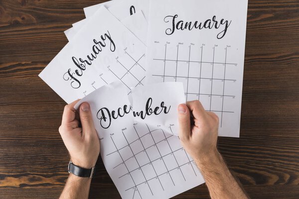 cropped shot of man tearing calendar on wooden tabletop