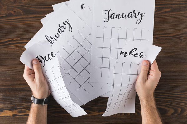 cropped shot of man tearing calendar on wooden tabletop