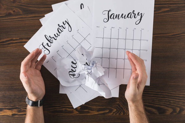 cropped shot of male hands and teared calendar on wooden tabletop