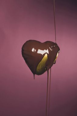 heart shaped candy in golden wrapper with pouring liquid chocolate isolated on pink