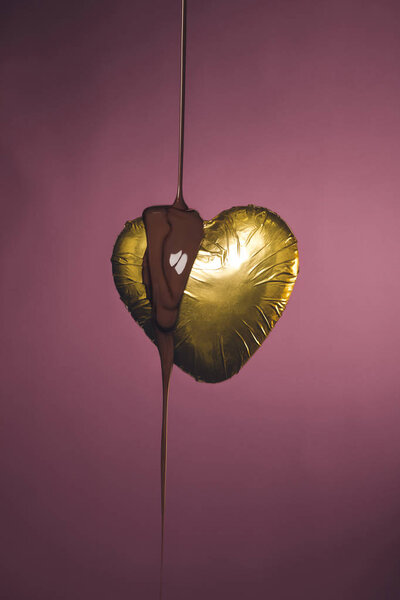 конфеты в форме сердца в золотой обертке с наливкой жидкого шоколада изолированы на розовый
