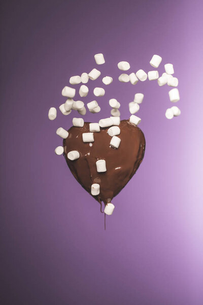 chocolate heart shaped candy with falling marshmallow isolated on purple