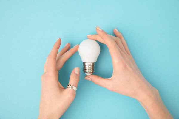 partial view of woman holding light bulb in hands isolated on blue