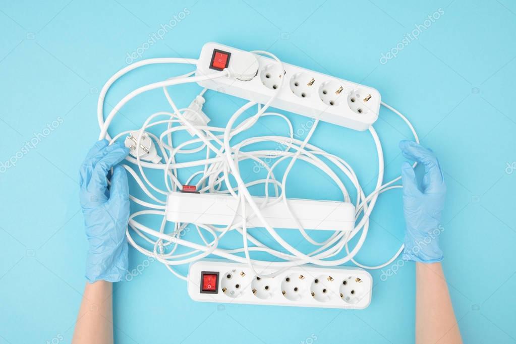 partial view of female hands in protective gloves and extension cords isolated on blue