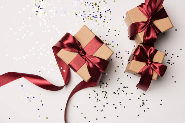 top view of arranged gifts with red ribbons and confetti isolated on white