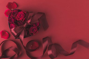 top view of roses in heart shaped gift box with ribbon and petals isolated on red, st valentines day holiday concept clipart