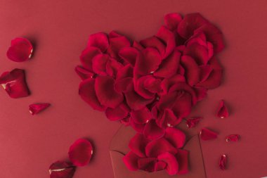 top view of heart made of roses petals and envelope isolated on red clipart