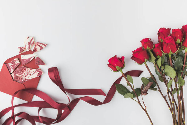 flat lay with arrangement of red roses with ribbon and envelope with sweet dessert isolated on white, st valentines day concept