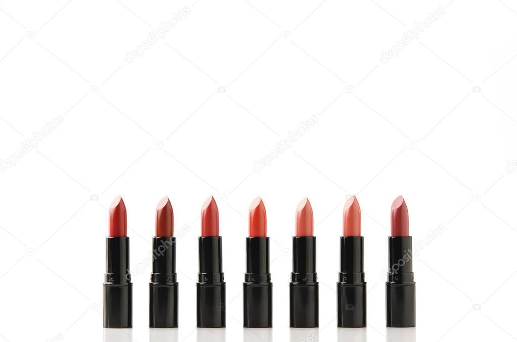 row of lipsticks of various shades in black tubes isolated on white