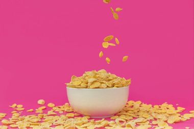 close-up view of sweet healthy corn flakes falling into white bowl on pink  clipart
