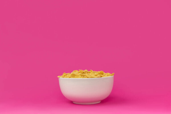 close-up view of white bowl with healthy tasty crunchy corn flakes isolated on pink