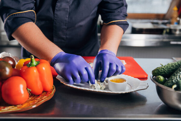 cropped shot of chef putting cheese slices on plate at kitchen