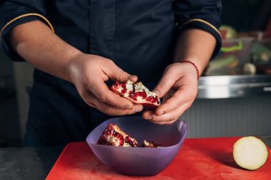 cropped shot of chef peeling pomegranate at kitchen of restaurant clipart