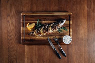top view of delicious grilled fish with lemon on wooden board clipart