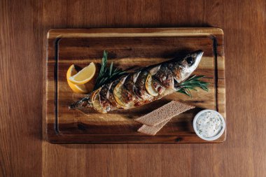 top view of grilled fish with lemon and rye bread on wooden board clipart